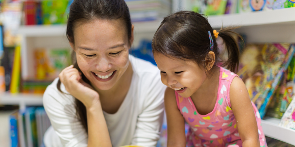 Mother and daughter, smiling as they look through a picture book at the Library