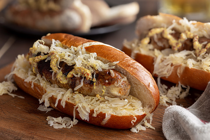 Closeup of grilled bratwurst with sauerkraut and dijon mustard on a bun