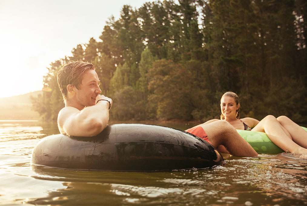 Portrait of happy young man in lake on inflatable ring with his girlfriend. Young couple relaxing in water on a summer day.